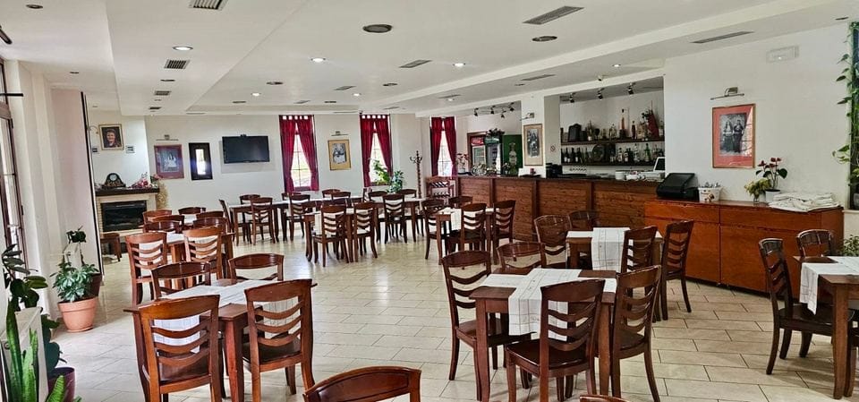 Salla e restorantit me karrige druri, mbulesa të bardha tavoline, oxhak dhe bar