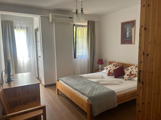 Camera matrimoniale con letto in legno, cuscini decorati e due finestre con tende leggere